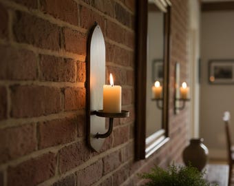 May include: A lit candle in a wall-mounted sconce against a red brick wall. The sconce has a metal candle holder and a wooden backplate. The warm light of the candle reflects in a nearby mirror.