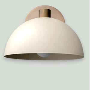 May include: Cream-colored dome-shaped wall sconce with a brass-colored mounting plate and a cylindrical fixture. The light fixture has a simple, modern design, suitable for various interior styles. The light bulb is visible at the bottom of the dome.