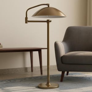 May include: A brass floor lamp featuring a domed shade and an adjustable arm. The lamp has a circular base and a straight pole. The shade is positioned above a grey armchair. The lamp is in a room with a wooden table and a patterned rug.