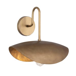 May include: A brass-toned wall sconce with a curved arm and a large, saucer-shaped shade. The shade has a warm, golden interior, and the fixture is mounted on a circular base. The design is modern and elegant, suitable for interior lighting.