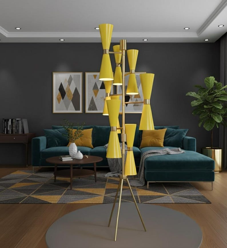 May include: A tall, modern floor lamp with a brass finish and multiple yellow cone-shaped shades. The lamp stands on a tripod base and illuminates a living room with a teal sofa, geometric rug, and artwork. The lamp's height is approximately 72 inches.