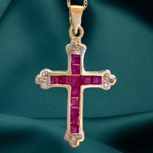 Pode incluir: Um colar com pingente dourado com um design de cruz. A cruz é adornada com pedras preciosas rosa vibrantes de corte quadrado e pequenas pedras de acento transparentes. O pingente pende de uma delicada corrente dourada.