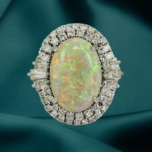 May include: An oval-shaped ring featuring a large opal gemstone with a shimmering, iridescent play of color. The opal is surrounded by a halo of small, sparkling diamonds set in a silver or white gold band.