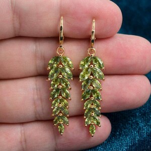 Puede incluir: Un par de pendientes colgantes de tono dorado con una disposición vertical de piedras preciosas de color verde claro talladas en marquise. Cada pendiente tiene un cierre de palanca y una estructura en cascada con forma de hoja de piedras facetadas.