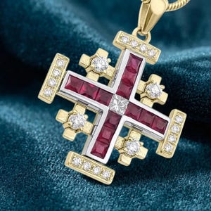May include: A gold Jerusalem cross pendant featuring square-cut deep red rubies set in the center and four arms. The cross is accented with small round white diamonds along the outer edges and at the four corners of the central cross structure.