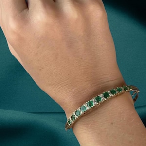 Peut inclure: Un bracelet doré orné d'une série de pierres précieuses vertes vives. Le bracelet présente de multiples émeraudes rondes, formant une ligne continue de couleur. Le design est élégant et adapté aux occasions spéciales.
