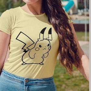 May include: A light yellow t-shirt featuring a black outline of an angry Pikachu character. The shirt is paired with blue denim jeans. The image also includes the text "AI SVG EPS DXF PNG".