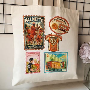 May include: Cream-colored tote bag featuring several colorful graphic designs. Designs include a lacrosse team, a cassette tape, a jersey with the number 03, and a building with the text "PSU FOXES".