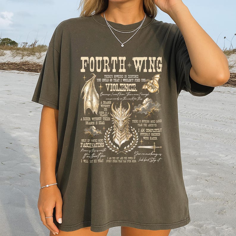 May include: A charcoal gray short-sleeve t-shirt featuring a graphic print with the text Fourth Wing and Violence, accompanied by illustrations of a dragon head, dragon wings, a sword, and clouds, with additional small text quotes.