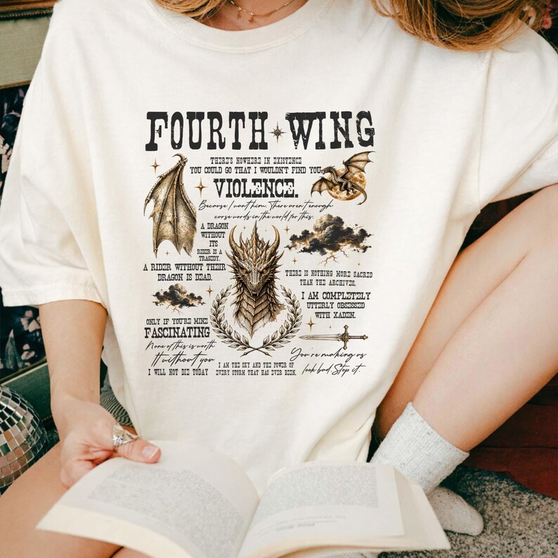 May include: An off-white short-sleeve t-shirt featuring a black graphic print with the text Fourth Wing and Violence. The design includes illustrations of a dragon head, a dragon wing, a sword, clouds, and various quotes from the book series.