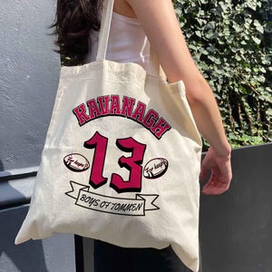 May include: Cream-colored tote bag with the name "KAVANAGH" in red and black lettering. The number "13" is in red, with "For keeps?" on either side. The words "BOYS OF TOMMEN" are on a banner.