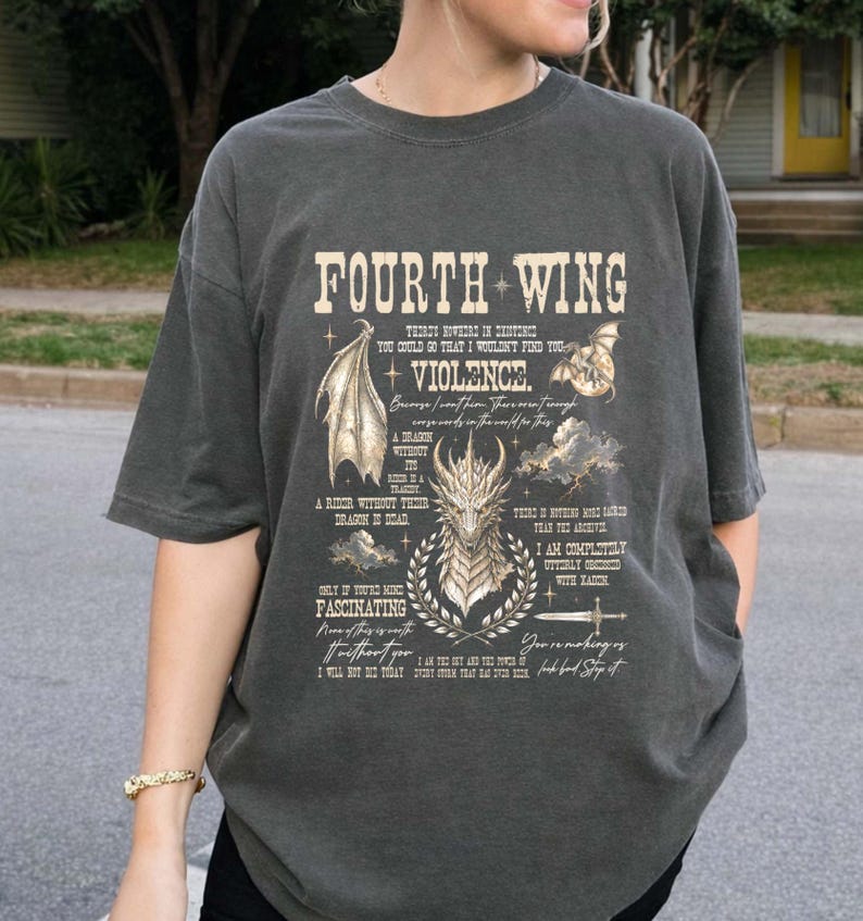 May include: A charcoal gray short-sleeve t-shirt featuring a graphic print with the text "FOURTH WING" and "VIOLENCE." The design includes illustrations of a dragon head, a dragon wing, clouds, a sword, and various quotes in a vintage style.