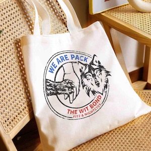May include: White tote bag with a circular graphic featuring a wolf's head and the text "WE ARE PACK" in blue and "THE WIT BOND" in red. The bag has two white handles.