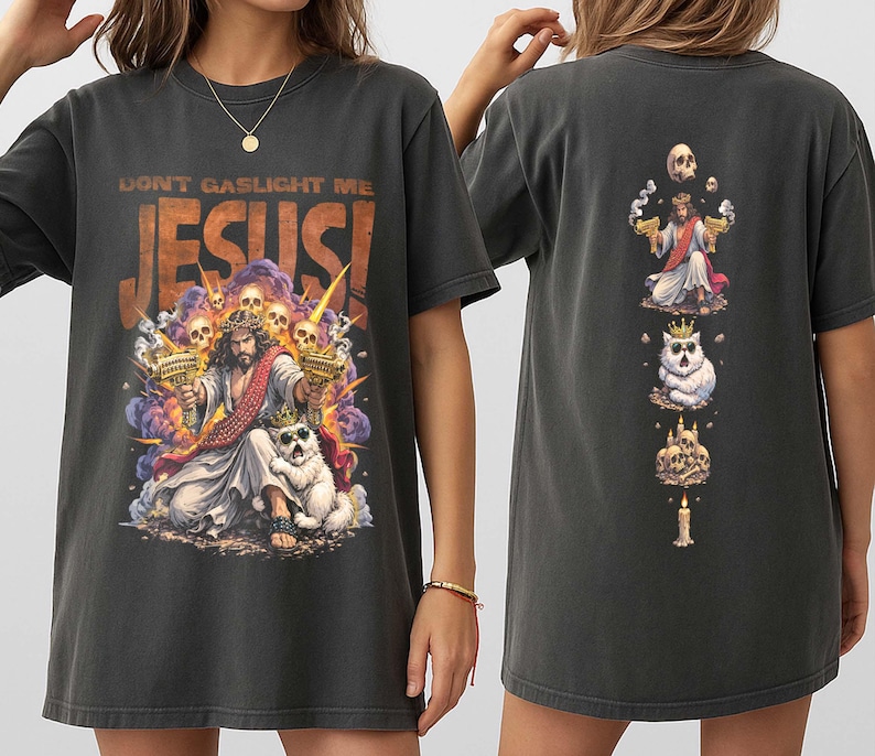K&ouml;nnte beinhalten: Dunkelgraues T-Shirt mit einem farbenfrohen Grafik von Jesus, der zwei goldene Pistolen h&auml;lt, mit dem Text "DON'T GASLIGHT ME JESUS!". Die R&uuml;ckseite des Shirts hat ein vertikales Design mit Jesus, einer Katze und einer Kerze.