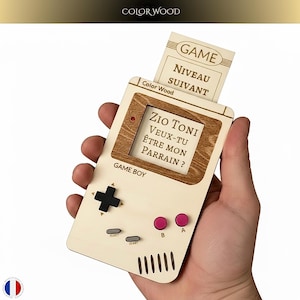 Peut inclure: Carte en bois en forme de Game Boy avec le texte "Zio Toni, veux-tu être mon parrain?" et "GAME NIVEAU SUIVANT". La carte a un corps crème avec des accents marron, une croix directionnelle noire, des boutons roses et le texte "GAME BOY".