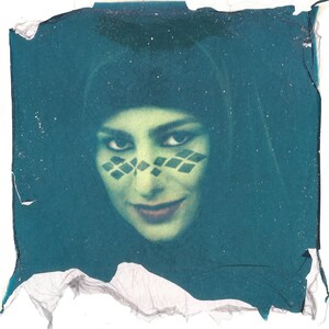 May include: A vintage-style portrait of a person with green skin and dark eyes, wearing a black head covering. The face features diamond-shaped markings around the eyes and a subtle smile. The image has a teal-colored border.