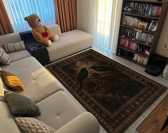 Könnte beinhalten: Ein rechteckiger Teppich mit einem dunklen, verzierten Design mit zwei schwarzen Vögeln, die auf einem Ast mit roten Rosen sitzen. Der Teppich liegt auf einem hellen Holzboden, in der Nähe eines beigen Ecksofas und eines Bücherregals.