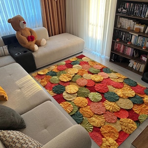 Puede incluir: Una colorida alfombra con un patrón floral en tonos rojos, naranjas, amarillos y verdes. La alfombra está en un salón con un sofá beige y una estantería llena de libros. Dimensiones aproximadas: 200 cm x 150 cm.