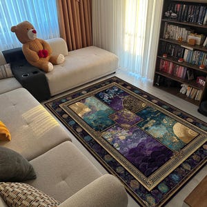 Op de afbeelding: Rechthoekig vloerkleed met een bloemen- en geometrisch patroon in tinten van teal, paars en goud. Het kleed heeft een omlijste rand en ligt op een houten vloer. Een beige bank en een teddybeer zijn op de achtergrond. Afmetingen ca. 200 cm x 300 cm.
