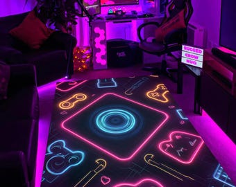 May include: A black gaming rug with a neon design featuring game controllers, hearts, and other gaming-related icons. The rug has a central circular design with a neon blue and pink glow. The words "RUGGED CROW RUG" are displayed on a sign.
