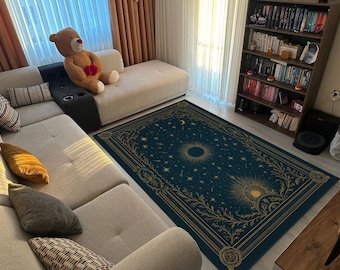 May include: A teal and gold area rug with a celestial design featuring a sun, moon, and stars. The rug is rectangular and placed on a hardwood floor in a living room setting. A beige sectional sofa and a teddy bear are also visible.