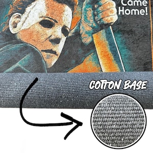 K&ouml;nnte beinhalten: Eine aufgerollte, dunkelgraue Fu&szlig;matte mit einem Nahaufnahme eines Horrorfilm-Charakters, der ein Messer h&auml;lt. Auf der Fu&szlig;matte steht "Cotton Base". Das Bild zeigt eine Nahaufnahme der Textur der Fu&szlig;matte.
