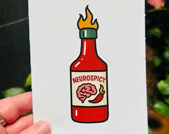 May include: A sticker featuring a red hot sauce bottle with flames at the top. The label reads "Neurospicy" and depicts a brain and a chili pepper. The sticker is held by a hand.
