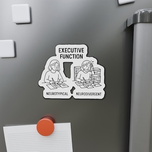 May include: A white magnet with a black and white illustration comparing "Neurotypical" and "Neurodivergent" executive function. The text "EXECUTIVE FUNCTION" is at the top. The magnet is on a gray surface with other magnets.