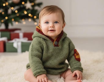 May include: A baby wearing a green knit hoodie with a red and yellow trim and a single button closure. The hoodie has a patch on the elbow. The baby is sitting on a white fluffy rug in front of a Christmas tree.
