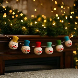 Pode incluir: Uma guirlanda de bonecos de neve de crochê, cada um com um chapéu de cor diferente. Os bonecos de neve têm rostos sorridentes com narizes vermelhos e olhos pretos. Os chapéus são amarelos, azuis, vermelhos, verdes e turquesas. A guirlanda está pendurada em uma superfície de madeira escura.
