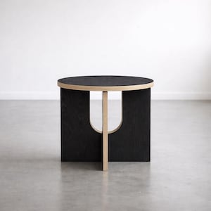 Puede incluir: Una mesa auxiliar negra moderna con una tapa redonda y un diseño de corte único. La mesa tiene un borde de madera natural y un único soporte central. La mesa mide aproximadamente 46 cm de diámetro y 46 cm de altura.
