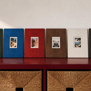 Pode incluir: Seis molduras retangulares de madeira nas cores verde-escuro, azul, vermelho, castanho, branco e preto, cada uma com uma textura de grão de madeira visível e uma pequena fotografia centrada, dispostas numa fila horizontal.