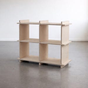 May include: A light-coloured wooden bookshelf with six cubbyhole shelves. The shelves are arranged in two rows of three, with vertical dividers creating the cubbyholes. The bookshelf is made of light-coloured wood and sits on a simple base.