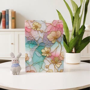 Könnte beinhalten: Ein dekoratives Notizbuch mit floralem Design. Das Cover hat einen Buntglaseffekt mit rosa, blauen und goldenen Akzenten. Goldfarbene Blumen und perlenartige Verzierungen sind über das Cover verstreut. Das Notizbuch ist rechteckig und steht aufrecht.
