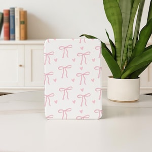 Könnte beinhalten: Ein weißes rechteckiges Objekt mit einem sich wiederholenden Muster aus rosa Schleifen und Herzen. Die Schleifen sind mit zarten Linien gezeichnet, und die Herzen sind klein und einfach. Das Objekt befindet sich auf einer weißen Oberfläche.