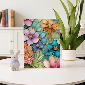 Könnte beinhalten: Ein rechteckiges Objekt mit einem farbenfrohen Blumendesign. Das Bild zeigt Blumen in Rosa, Orange, Blau und Lila, umrandet in Gold, vor einem hellen Türkis Hintergrund. Das Design ist detailliert und auffällig.