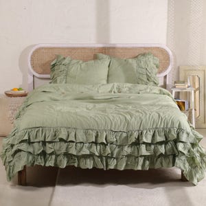 May include: Sage green bedspread with ruffled trim, two matching pillow shams, and a woven headboard. The bedding set is made of soft fabric and has a relaxed, inviting look. The bed is made up with a duvet cover and two pillows.