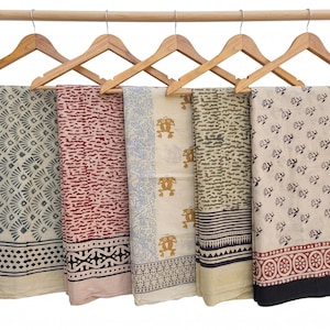 May include: Five rectangular fabric pieces with distinct block-printed patterns hanging on wooden hangers. The designs include grey fan shapes, red horizontal textures, yellow frog motifs, green textured stripes, and black floral patterns with borders.