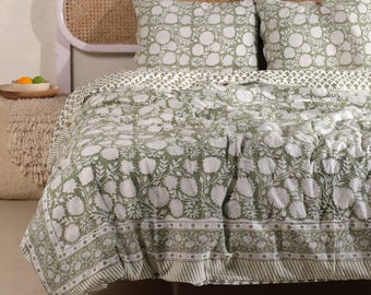 May include: A bed with a green and white floral patterned quilt and matching pillowcases. The quilt has a large floral design, with a striped border. The headboard is a light brown wicker material.