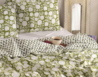 May include: A bed is made with a green and white floral patterned quilt and matching pillowcases. A wooden tray holds a cup of coffee and a small dish. A decorative mirror is in the background.