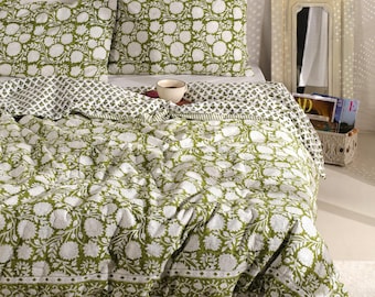May include: A bed covered with a green and white floral patterned quilt and matching pillowcases. The bedding features a repeating floral design. A small white bowl sits on the quilt. The room has a neutral color palette.