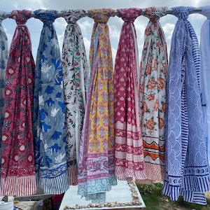 May include: A collection of colorful scarves hanging on a metal rod. The scarves feature various floral and geometric patterns in shades of blue, red, yellow, and white. The scarves are made of lightweight fabric, perfect for warm weather.