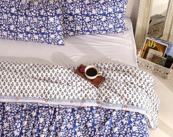 May include: A bed with a blue and white floral patterned duvet cover and two matching pillowcases. A cup of coffee sits on a wooden tray on the bed. The bedding has a botanical theme.