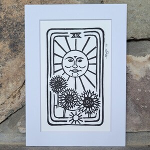 May include: A black and white illustration of the Sun tarot card, featuring a sun with a face and three sunflowers. The card number, XIX, is visible in the top right corner.