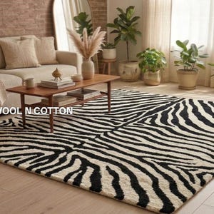 May include: A rectangular area rug featuring a high-contrast black and white zebra stripe pattern. The rug is positioned on a light-coloured wooden floor. The text WOOL N COTTON is visible on the surface of the rug in white capital letters.