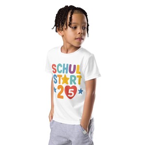 Puede incluir: Una camiseta blanca con las palabras "SCHUL START 25" en letras y números coloridos. El diseño incluye una estrella amarilla, un corazón rojo y estrellas azules. La camiseta la lleva un niño.