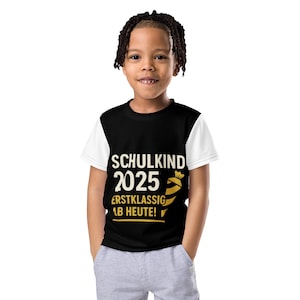 May include: A black and white t-shirt with the text "SCHULKIND 2025 ERSTKLASSIG AB HEUTE!" in white and gold. The shirt is worn by a child.