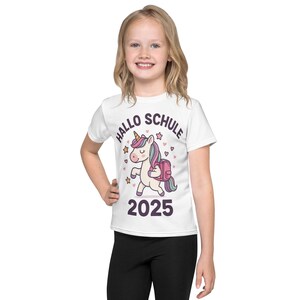 May include: White t-shirt featuring a cartoon unicorn with a backpack, stars, and hearts. The text "HALLO SCHULE 2025" is printed above and below the unicorn. The shirt is worn by a young person.