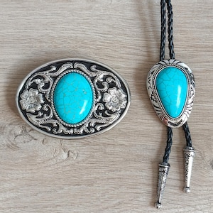 以下が含まれることがあります： シルバーカラーのベルトバックルとボータイのセット。どちらのアイテムも、中央に大きなターコイズ色の石が特徴です。バックルには花柄とスクロールワークのディテールがあります。ボータイは編み込みの黒いコードと装飾的なシルバーのチップが付いています。