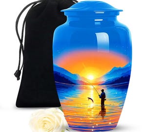 May include: A blue cremation urn with a scenic sunset and fishing scene. The urn has a glossy finish and is accompanied by a black velvet bag and a white rose. The artwork depicts a person fishing on a lake at sunset.